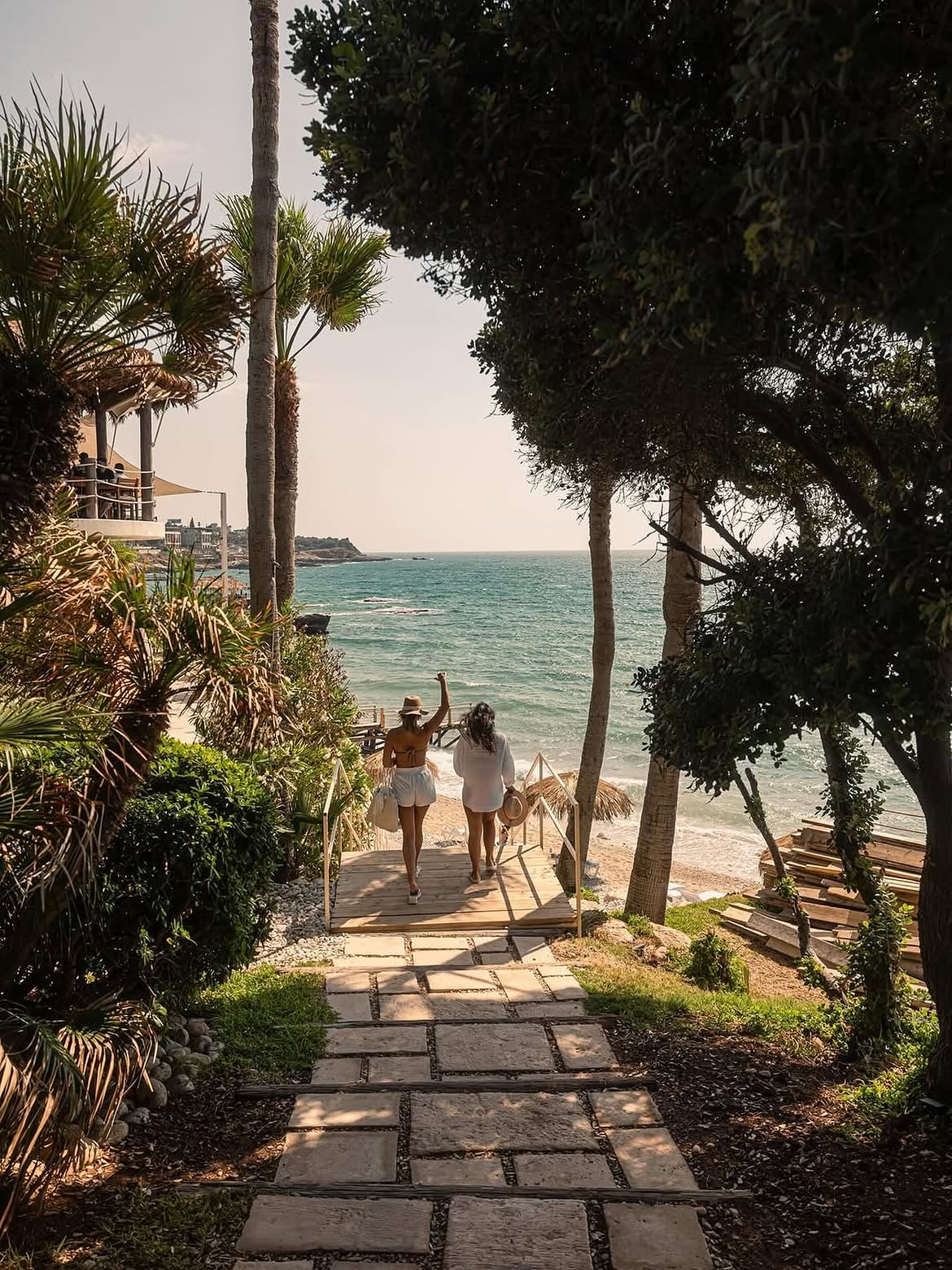 Two guests walking down a shaded stone path toward the turquoise sea at Bonita Bay